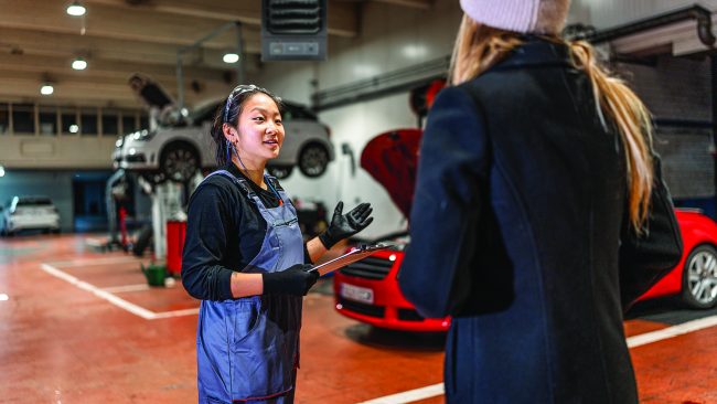 Professional female mechanic explaining car repair details to customer, holding clipboard in auto repair shop